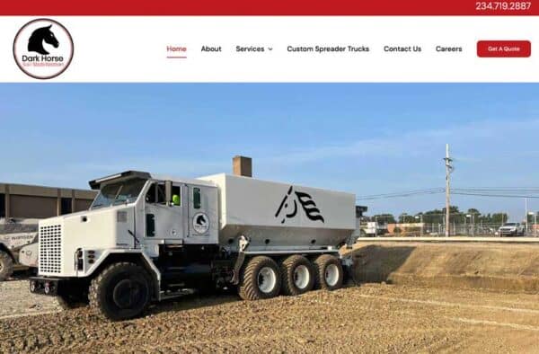 A large white custom spreader truck with a horse logo is parked on a construction site in front of buildings, beneath a clear sky. This impressive vehicle is featured in the Dark Horse company’s website portfolio, as shown by the logo and header.
