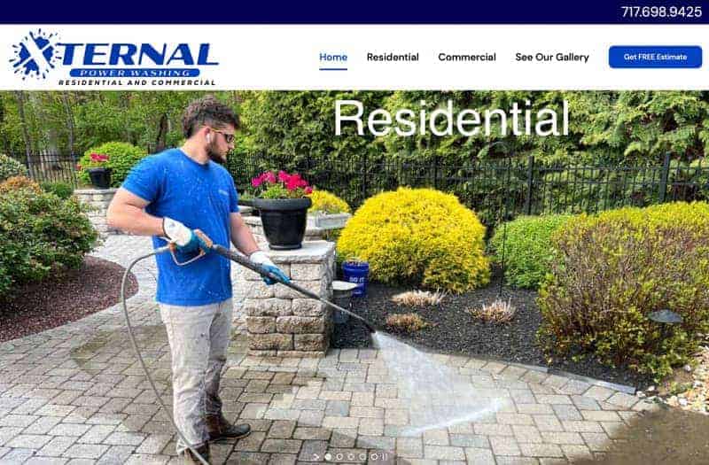 A man wearing gloves and a blue shirt uses a power washer to clean a stone patio in a landscaped yard. The image, perfect for your website portfolio, features the text Residential, promoting external power washing services.
